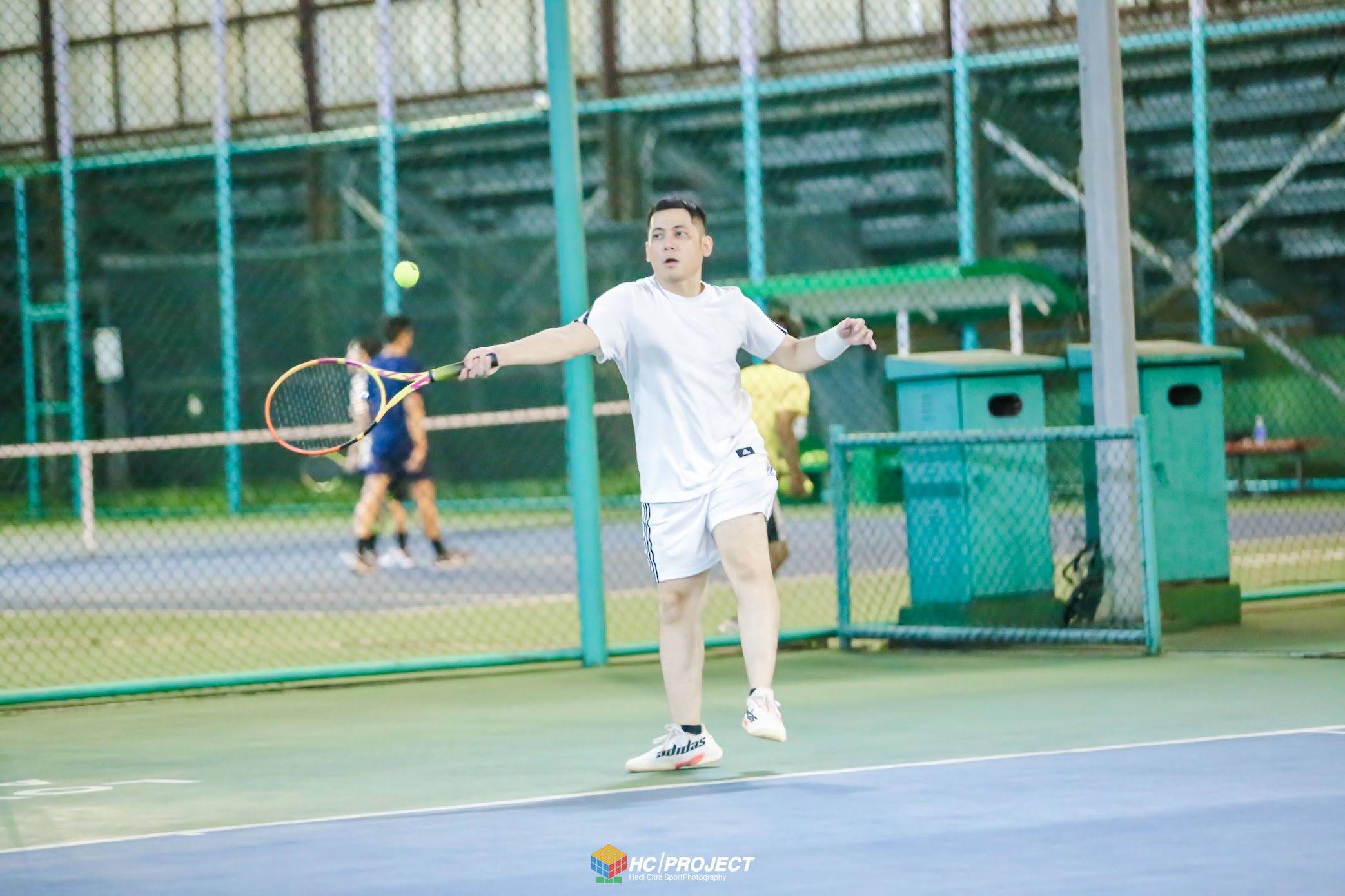 The author in white tennis clothes preparing a forehand on a covered court.