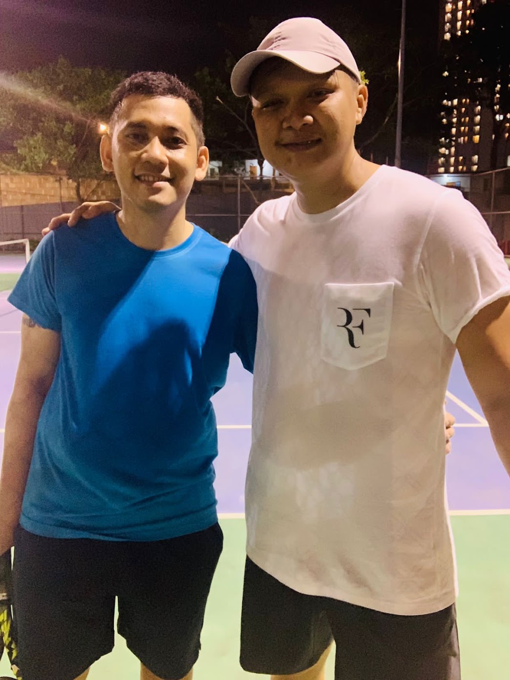 Me in a light-blue shirt, standing beside my opponent on the tennis court at night.